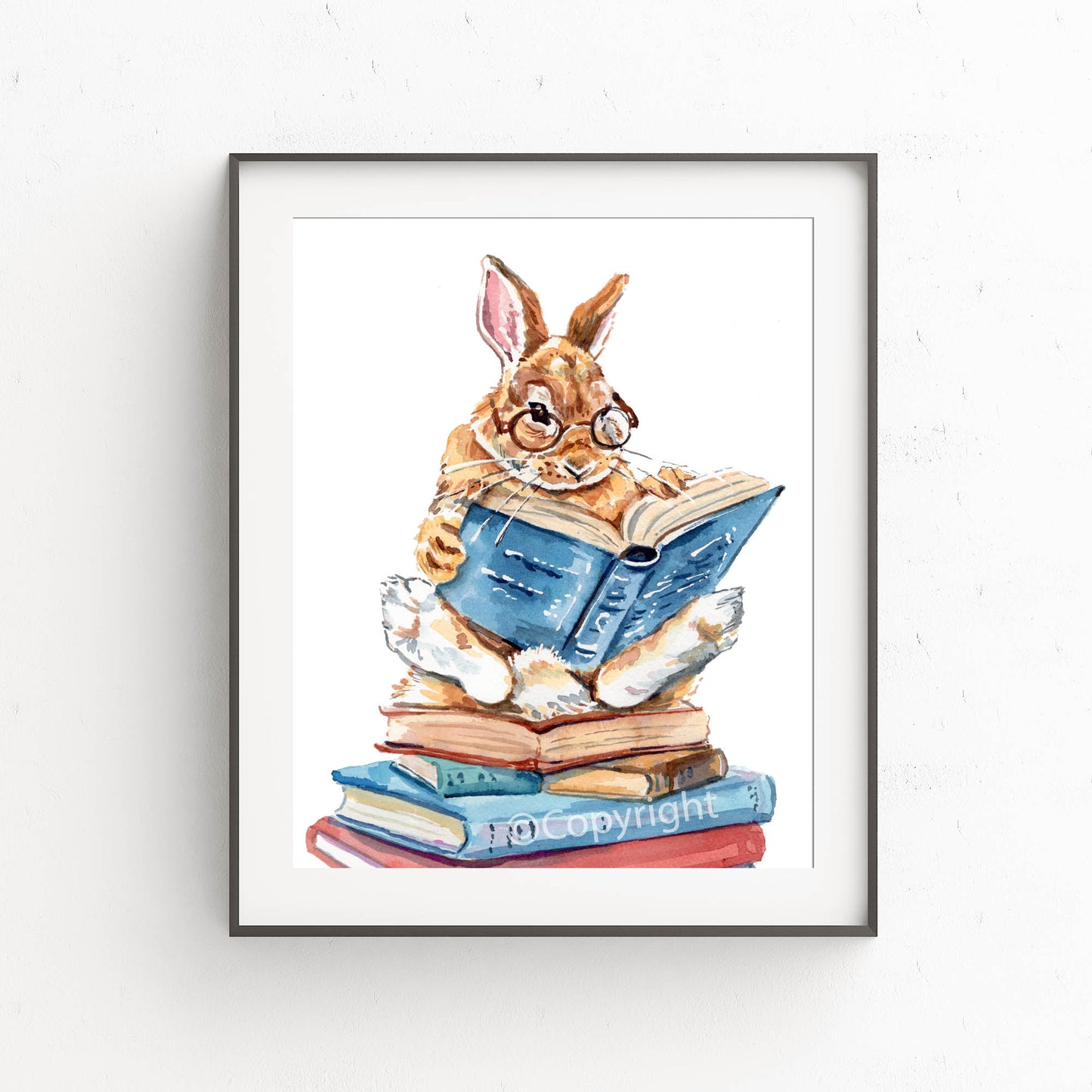 Framed artwork of a rabbit reading a book on a stack of books.