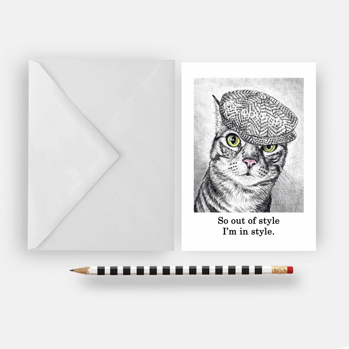 Blank greeting card featuring a black and white wax pastel drawing of tabby cat wearing a cap. Art by Deidre Wicks