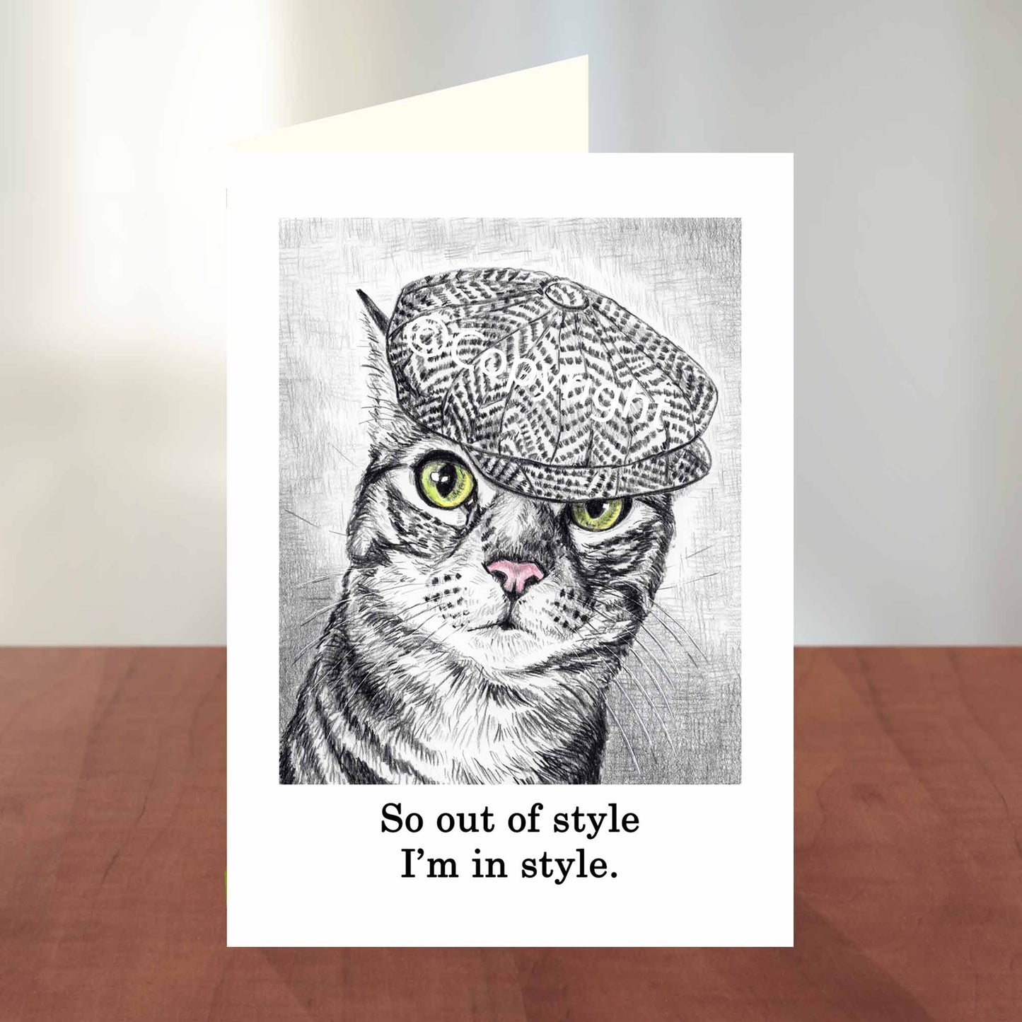 Blank greeting card featuring a black and white wax pastel drawing of tabby cat wearing a cap. Art by Deidre Wicks