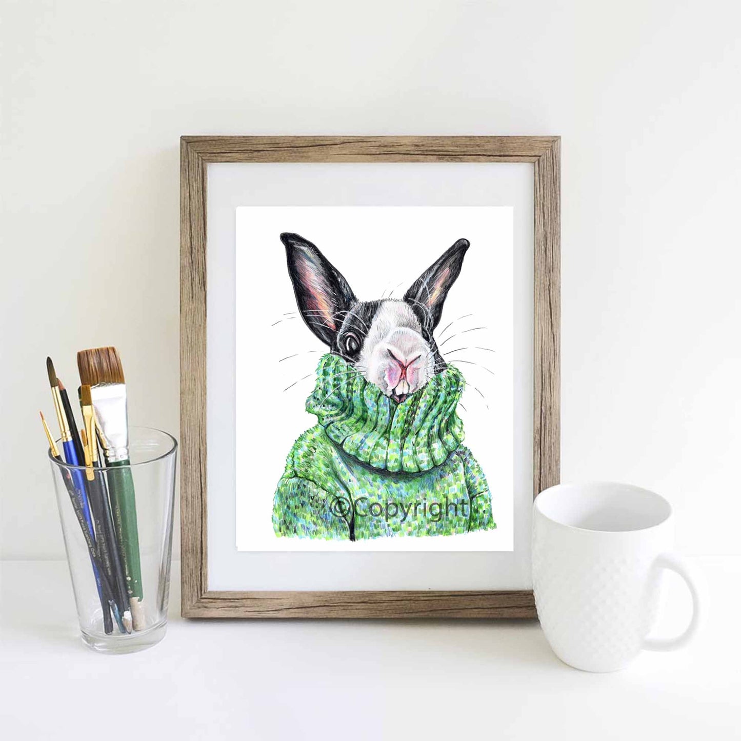 Coloured pencil drawing of a black and white bunny rabbit wearing a large green sweater. Art by Deidre Wicks
