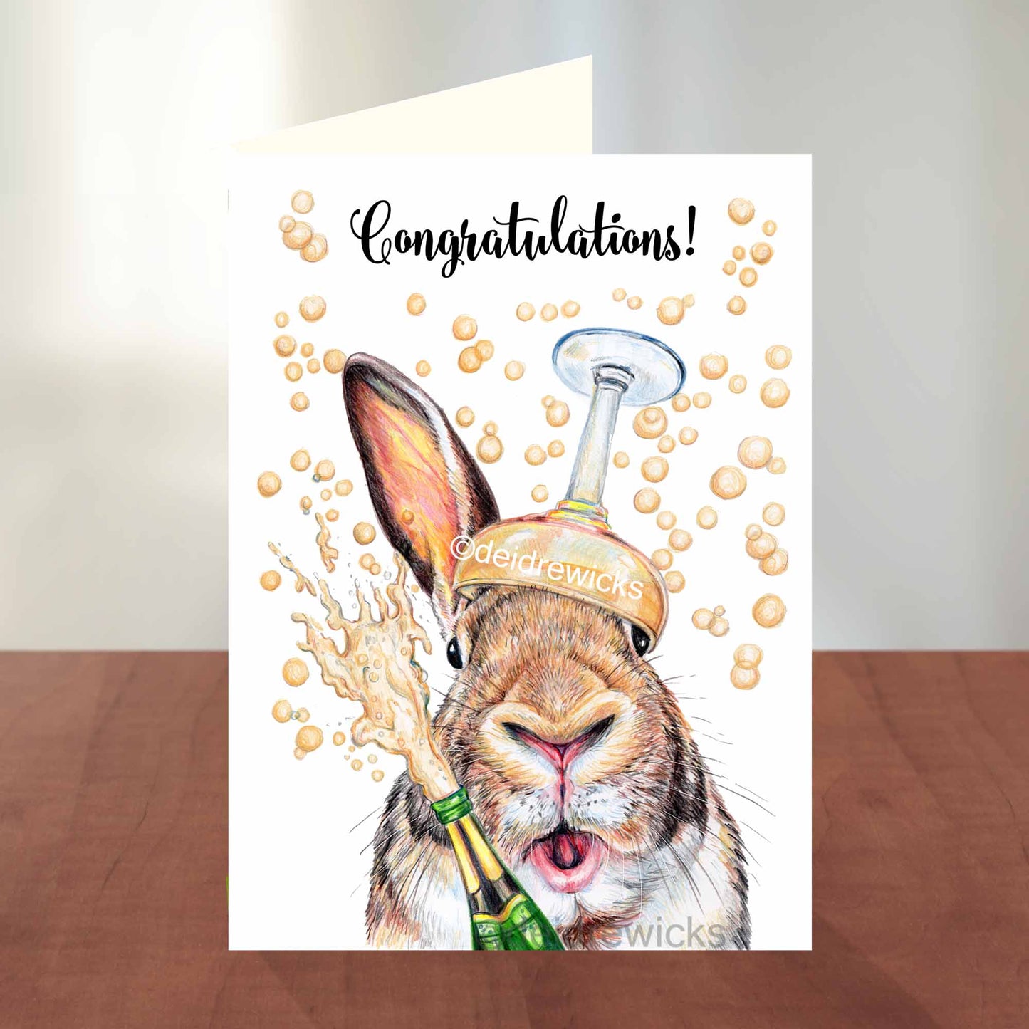 Congratulations greeting card featuring a bunny rabbit with a sparkling bottle of wine and a glass. By Deidre Wicks