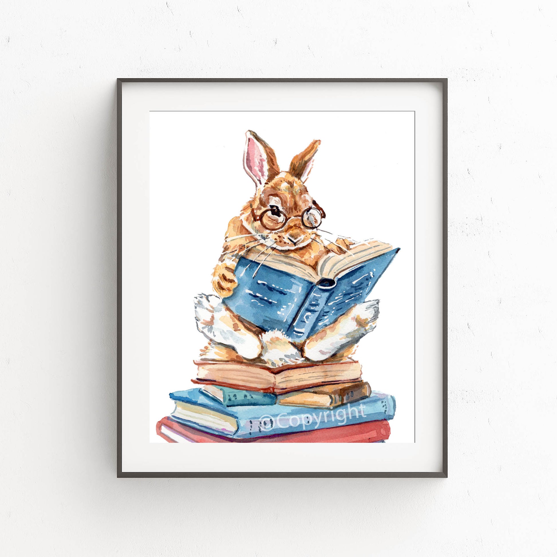 Framed artwork of a rabbit reading a book on a stack of books.