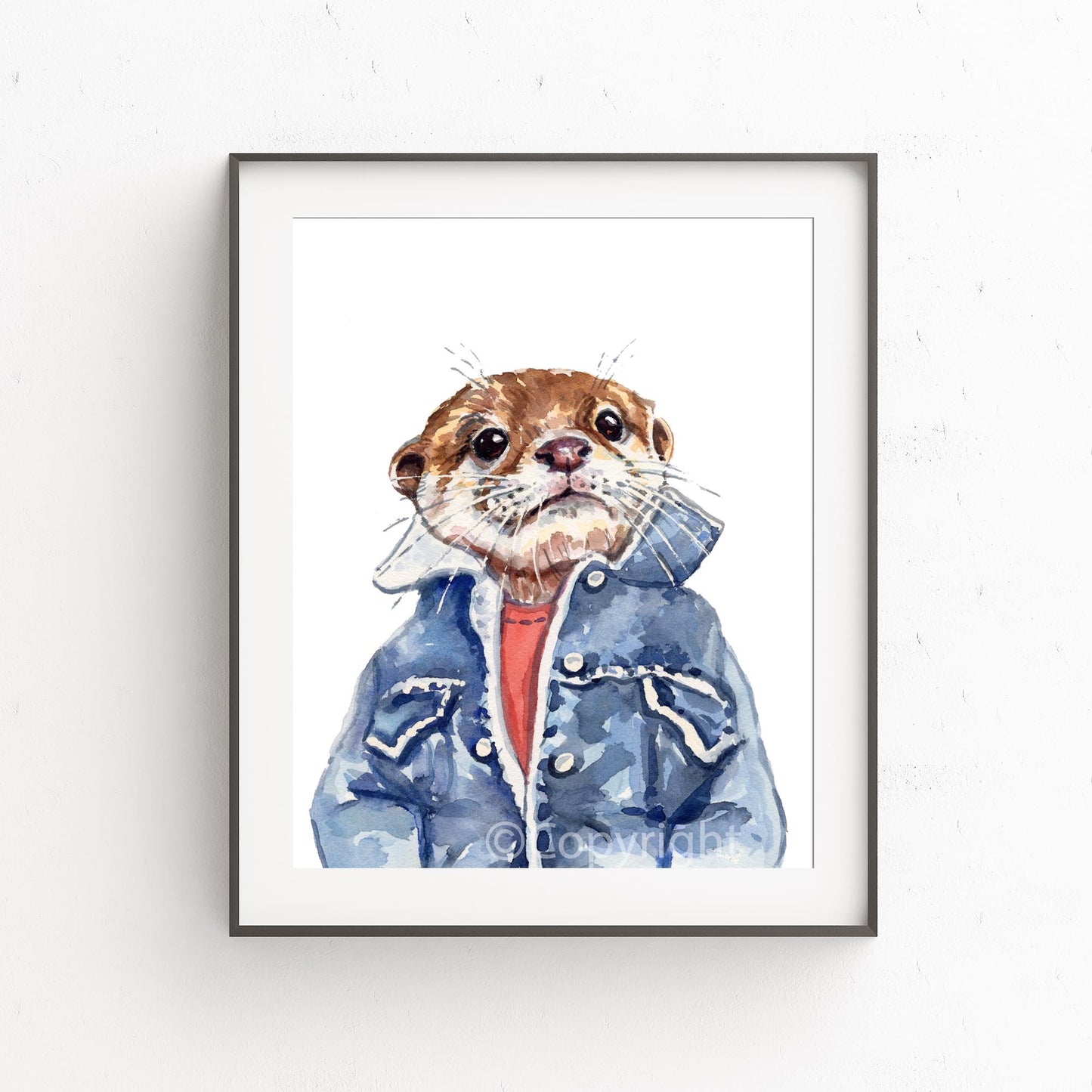 A framed watercolor art print of an otter wearing a blue denim jacket and red shirt, displayed on a white textured wall.