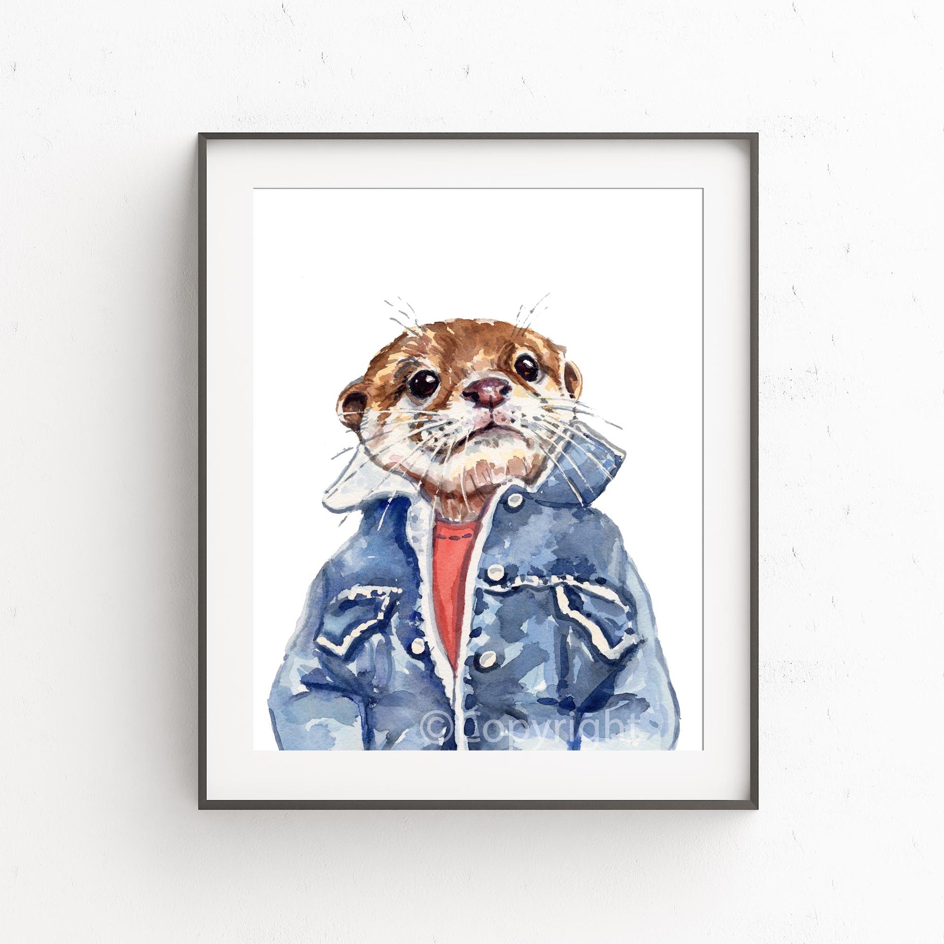 A framed watercolor art print of an otter wearing a blue denim jacket and red shirt, displayed on a white textured wall.
