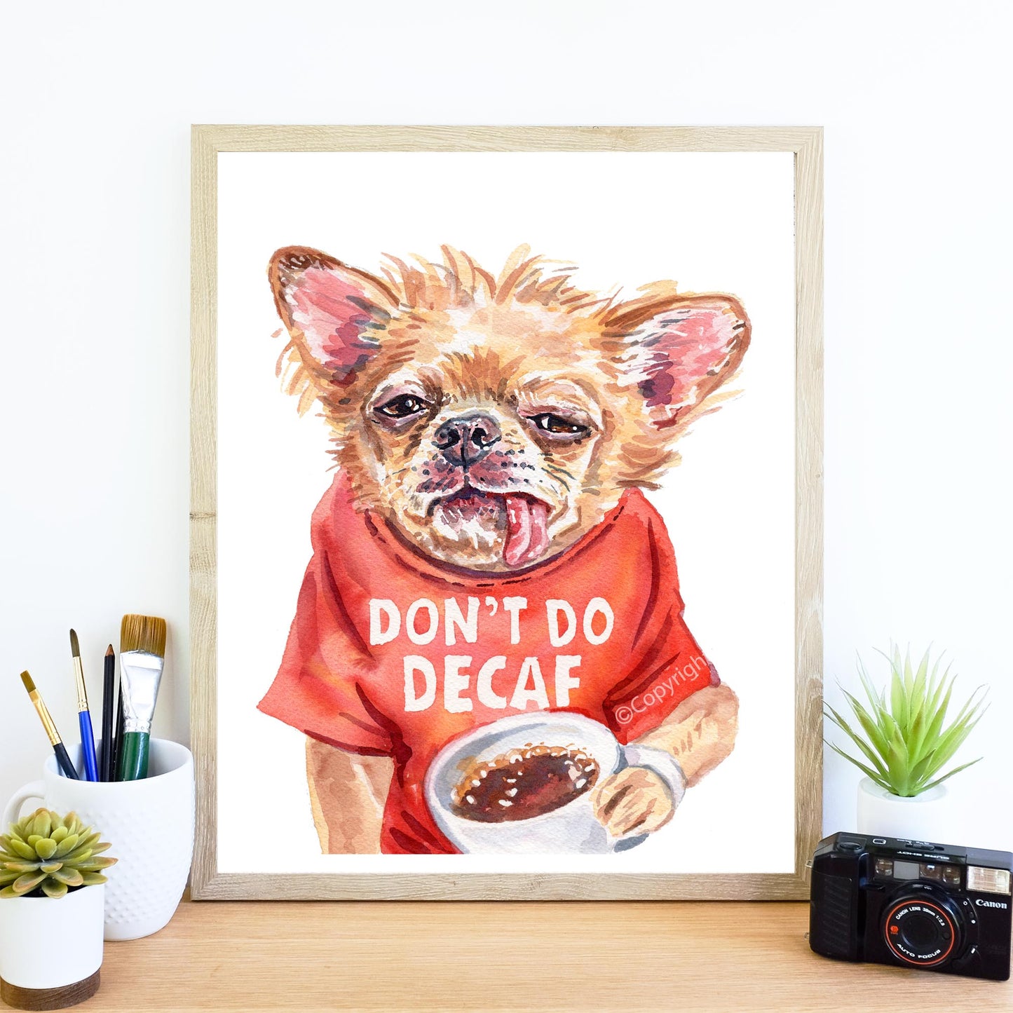 Framed artwork of a dog wearing a red shirt with 'Don't Do Decaf' text, holding a cup of coffee.