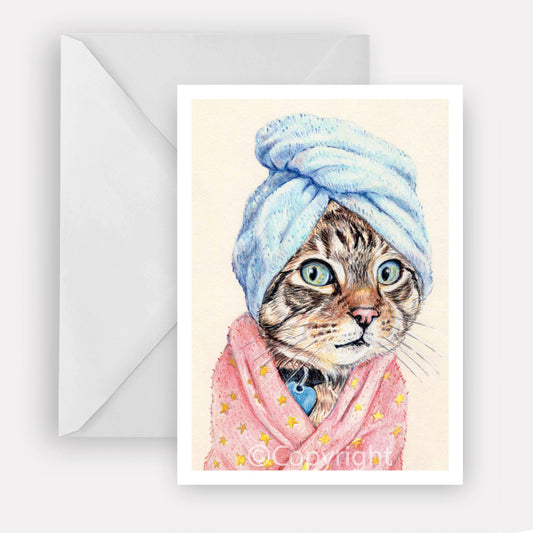 Greeting card featuring a coloured pencil drawing of a brown tabby cat wearing a bath towel and fuzzy pink bath robe. Art by Deidre Wicks