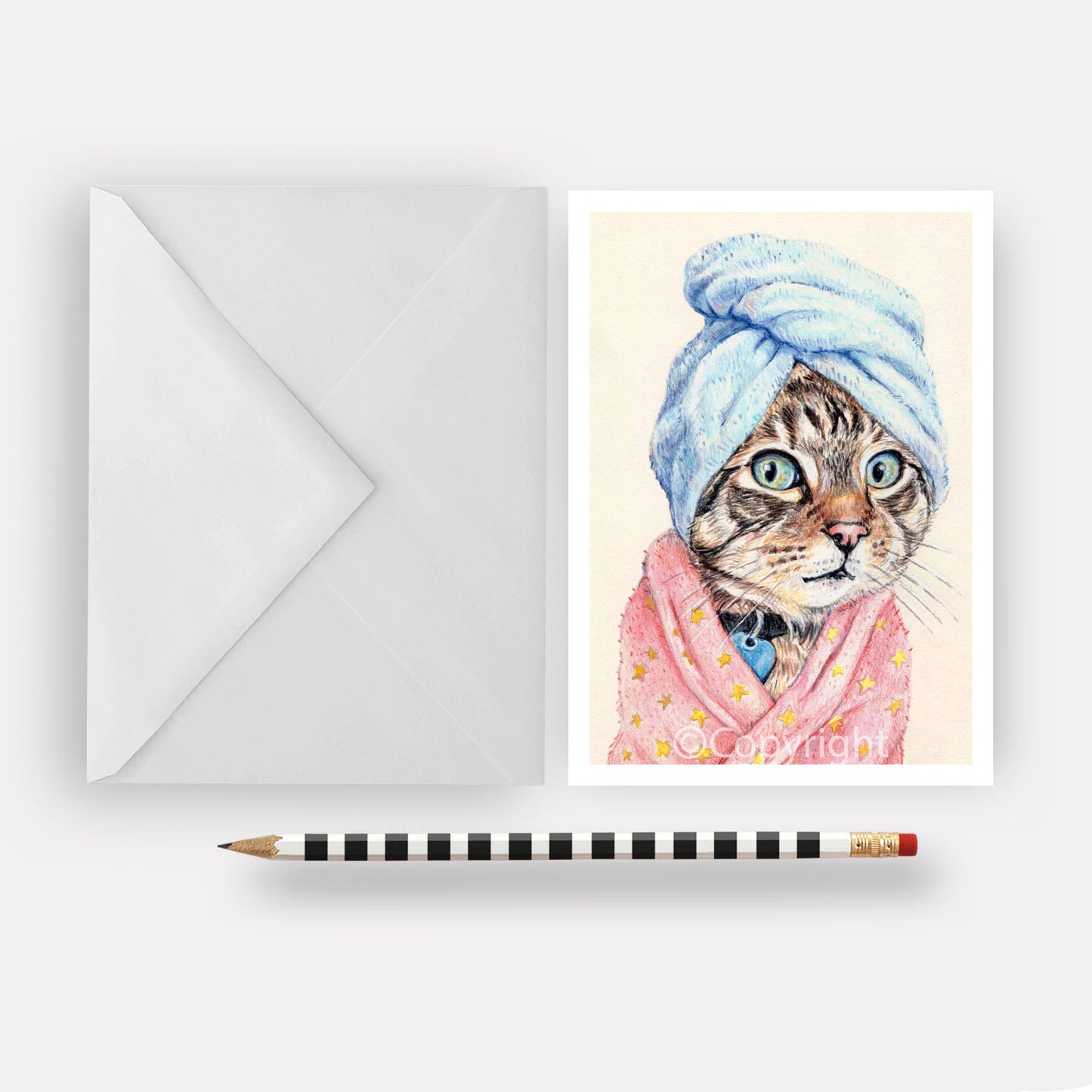 Greeting card featuring a coloured pencil drawing of a brown tabby cat wearing a bath towel and fuzzy pink bath robe. Art by Deidre Wicks