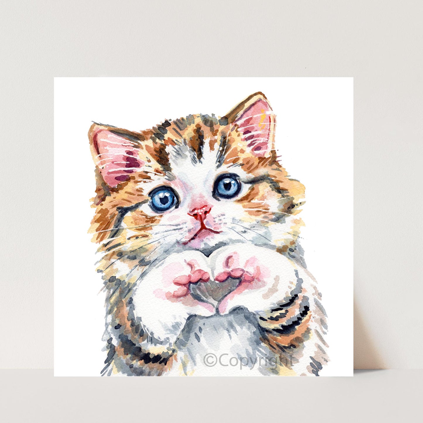 Watercolor painting of a calico cat with blue eyes forming a heart with his paws on a white background