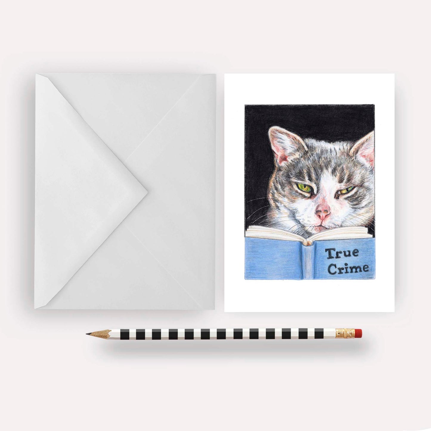 Greeting card featuring a coloured pencil drawing of a grey tabby cat reading a book about true crime. Art by Deidre Wicks