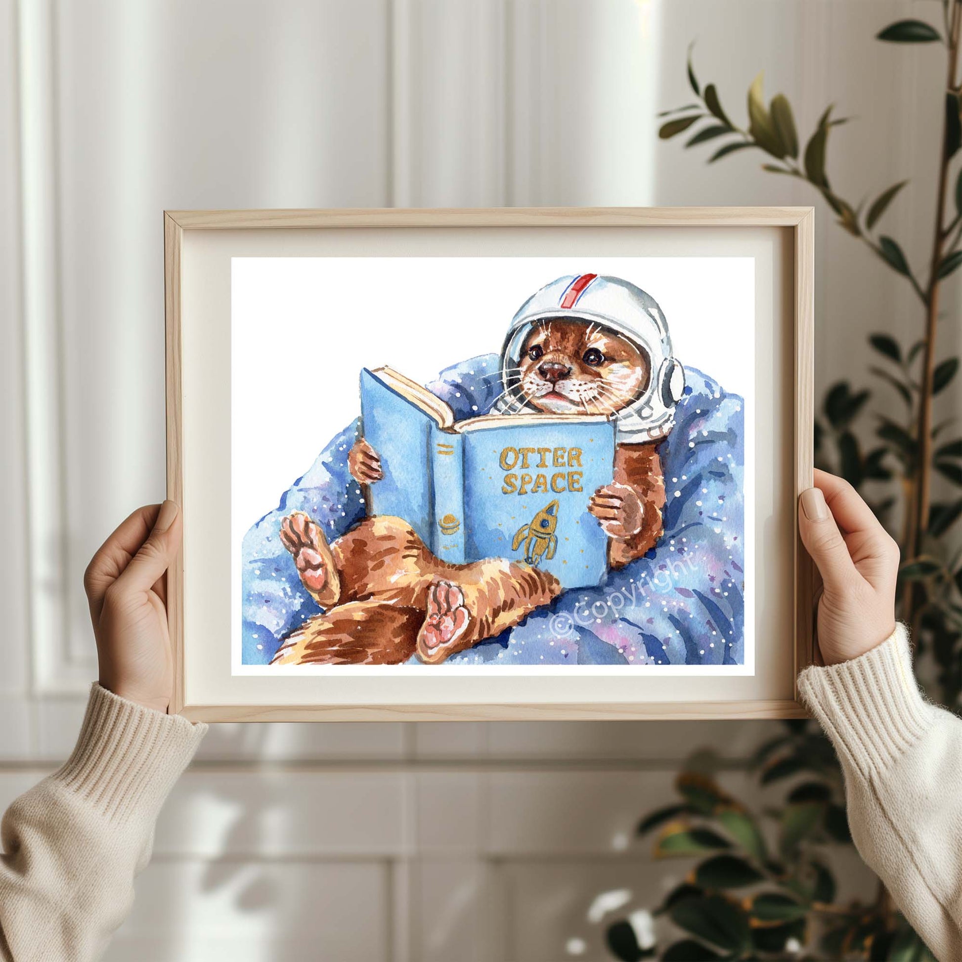 Framed artwork of an otter in an astronaut suit reading a book titled 'Otter Space'.