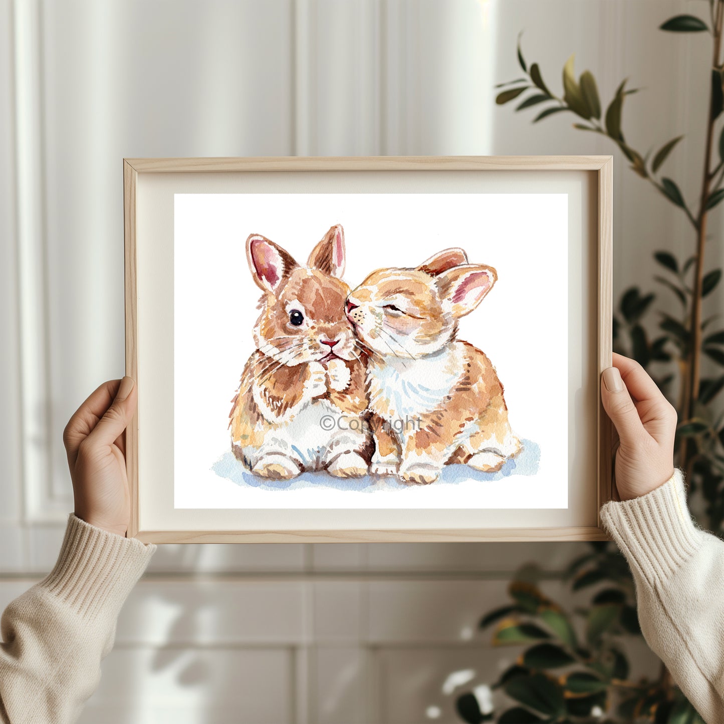 Framed artwork of two rabbits held by a person against a neutral background