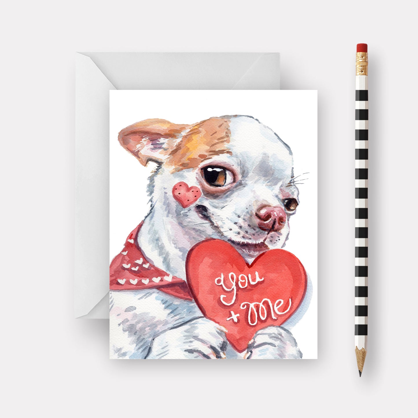 Card with a dog holding a heart that says 'You + Me' next to a pencil on a white background