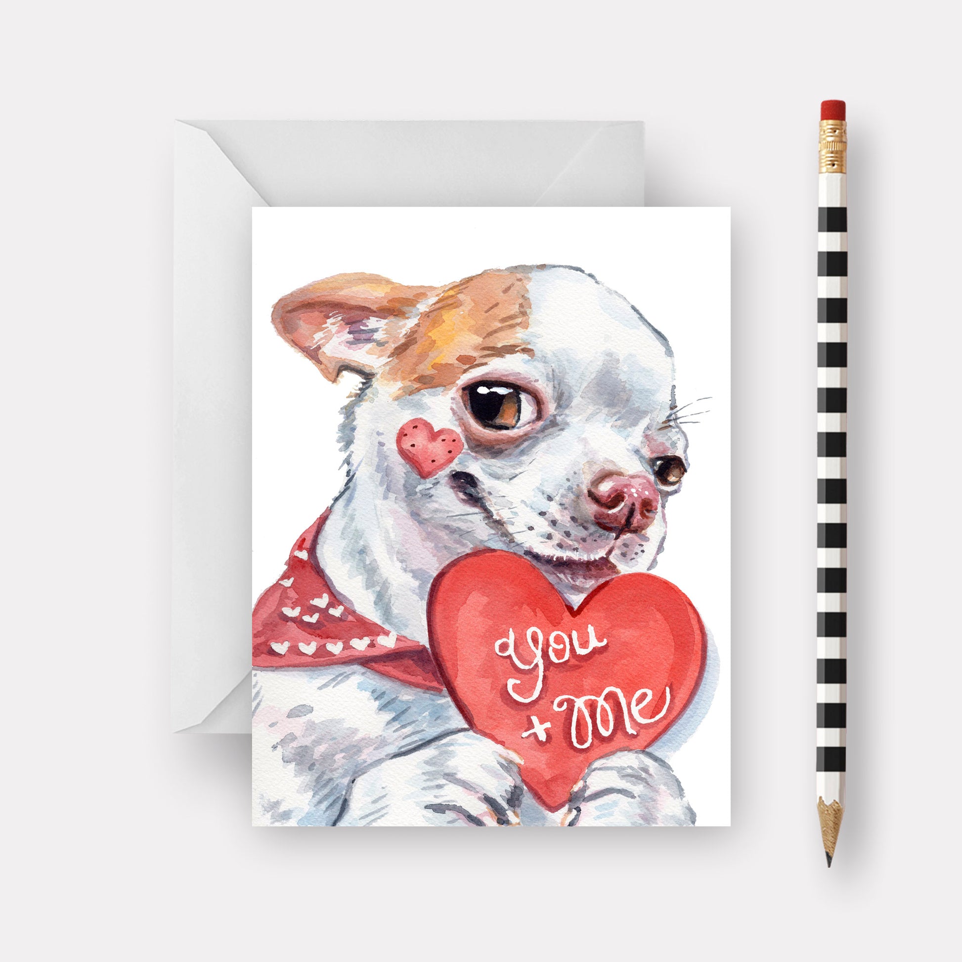 Card with a dog holding a heart that says 'You + Me' next to a pencil on a white background