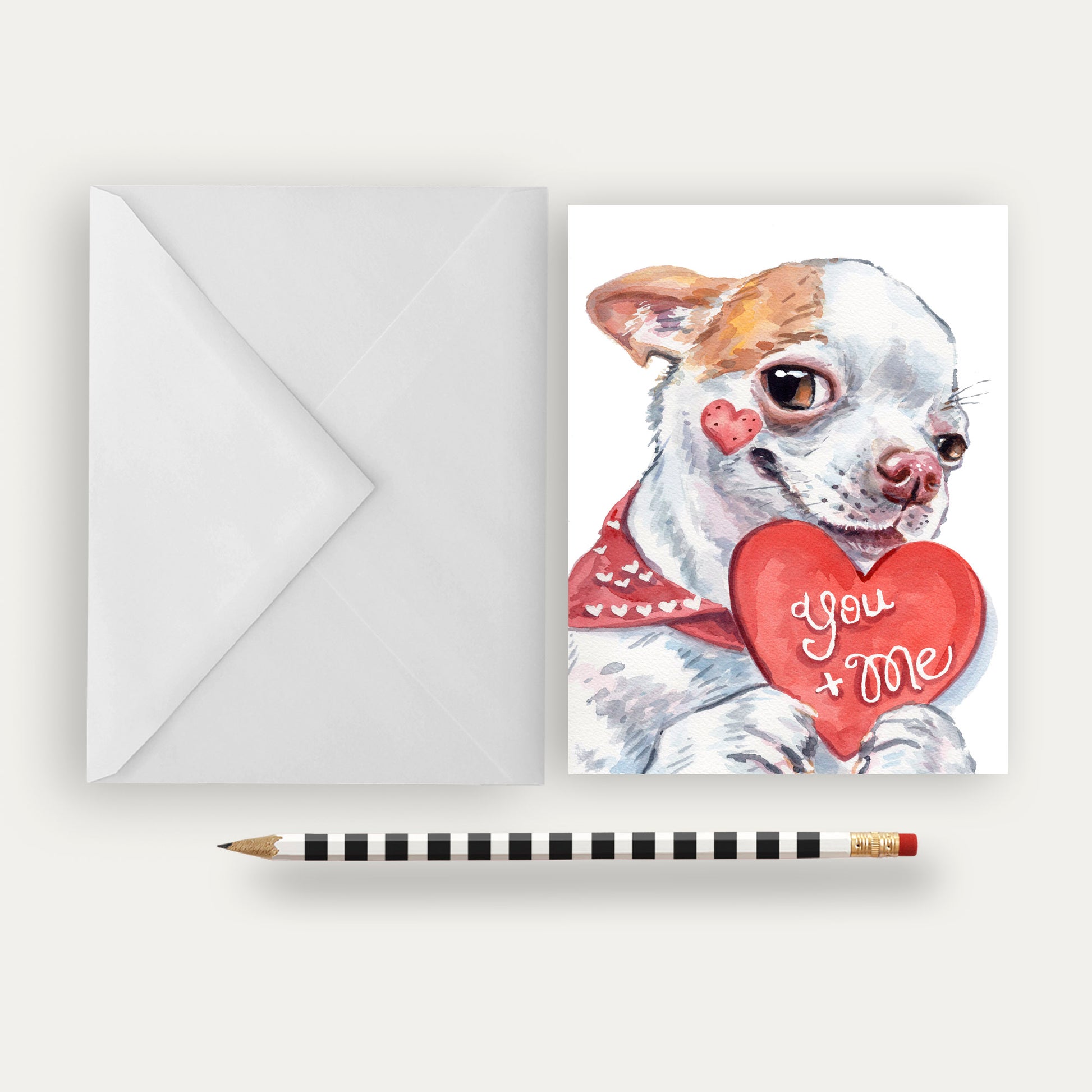 Greeting card with a dog holding a heart-shaped 'You + Me' card, envelope, and pencil on a white background