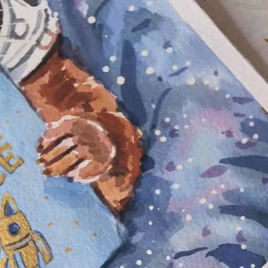 Video of watercolour painting of an otter with a space helmet reading a book about Otter Space