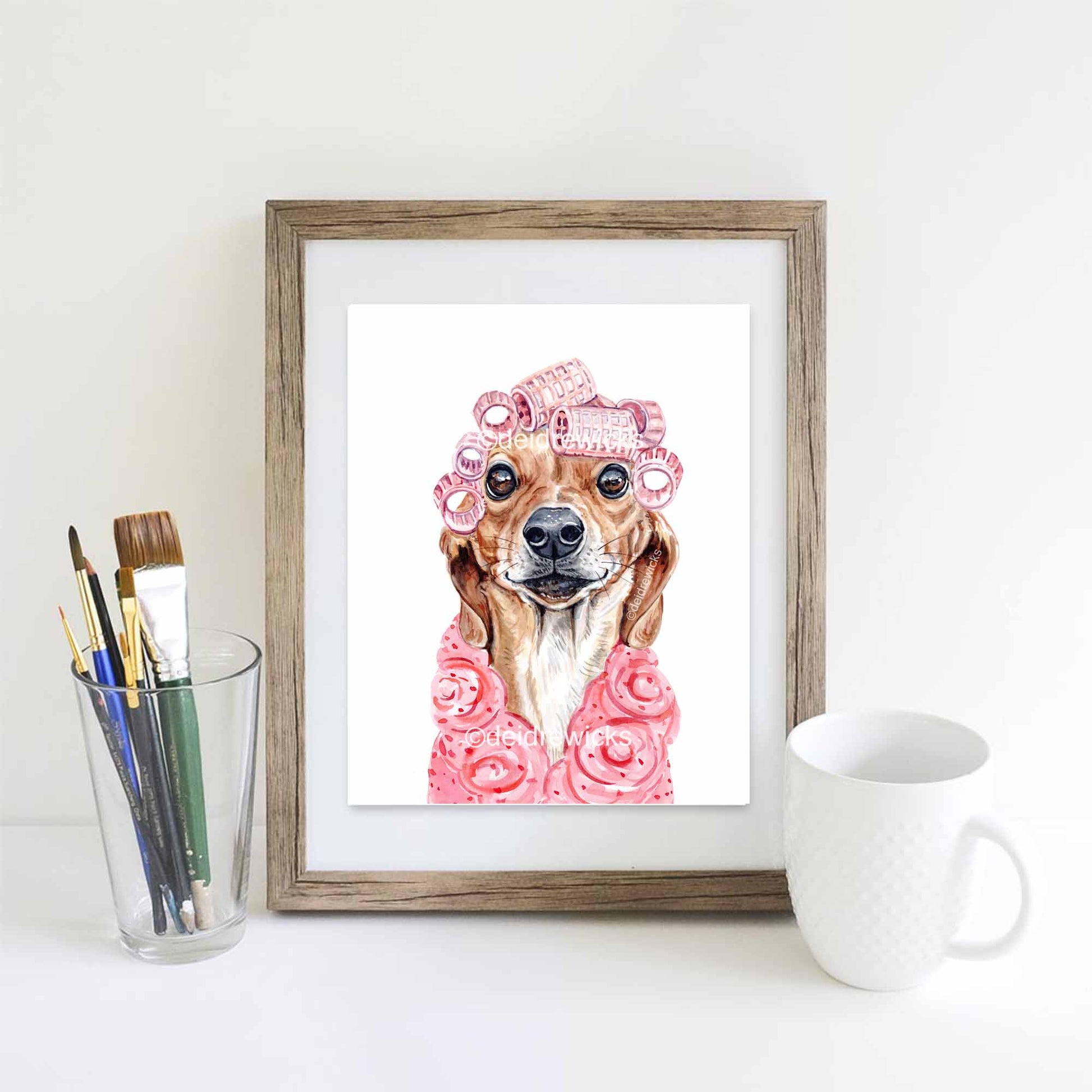 Framed watercolour painting of a dachshund dog wearing a pink bathrobe and hair curlers by artist Deidre Wicks