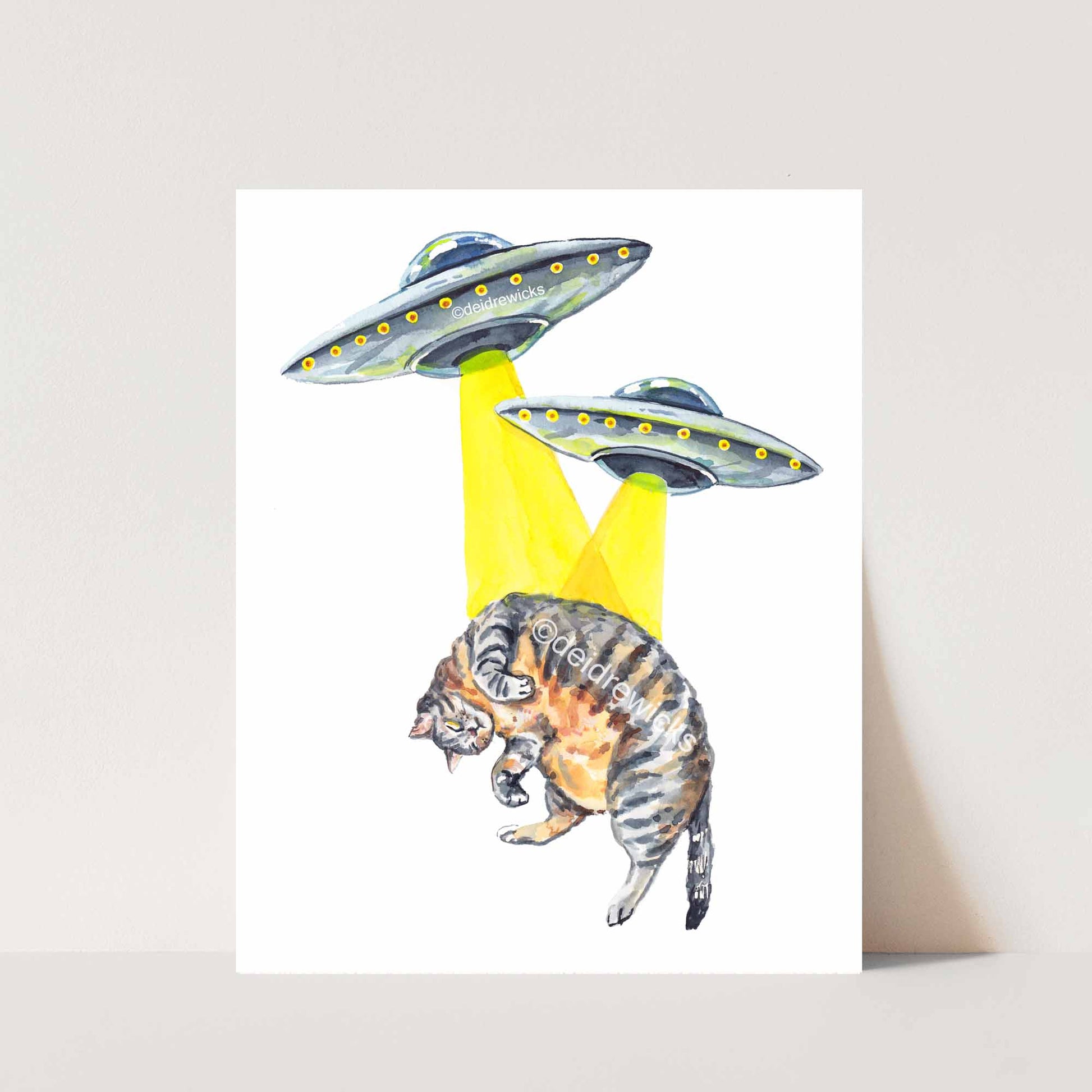 Watercolour print featuring two small ufos trying to abduct a fat brown tabby cat. By Deidre Wicks