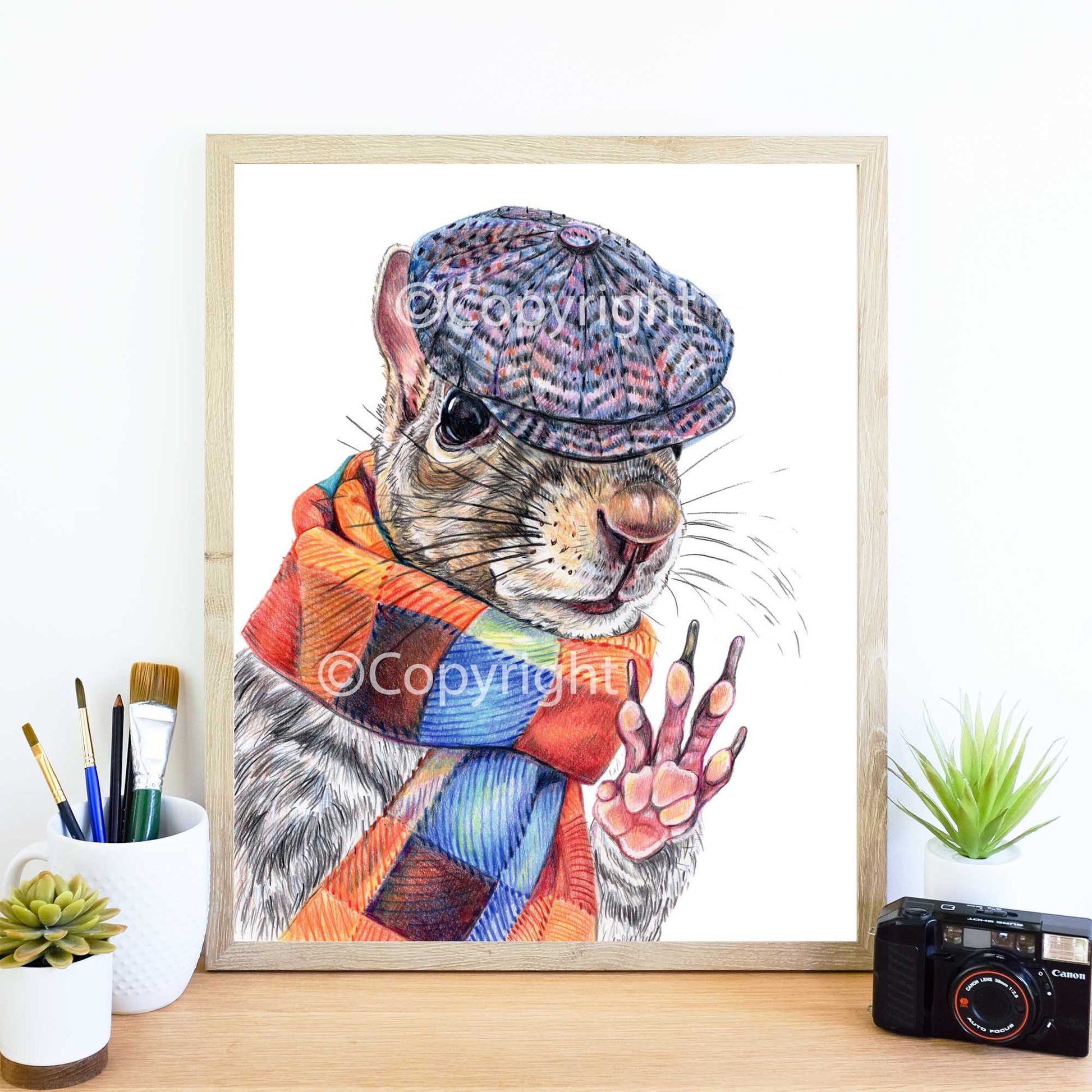 Coloured pencil drawing of a dapper Eastern grey squirrel wearing a newsboy hat and wool scarf. Art by Deidre Wicks