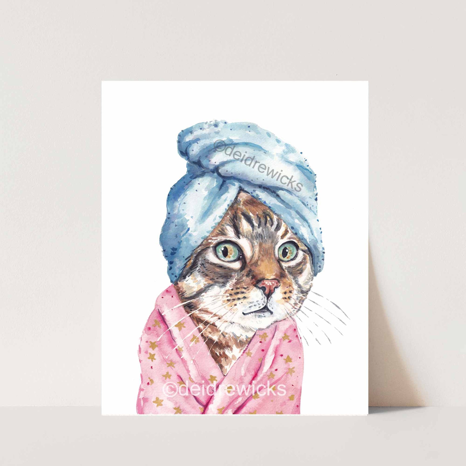 Watercolor print of a brown tabby cat wearing a bath towel on it's head and a soft, pink bathrobe. Copyright Deidre Wicks