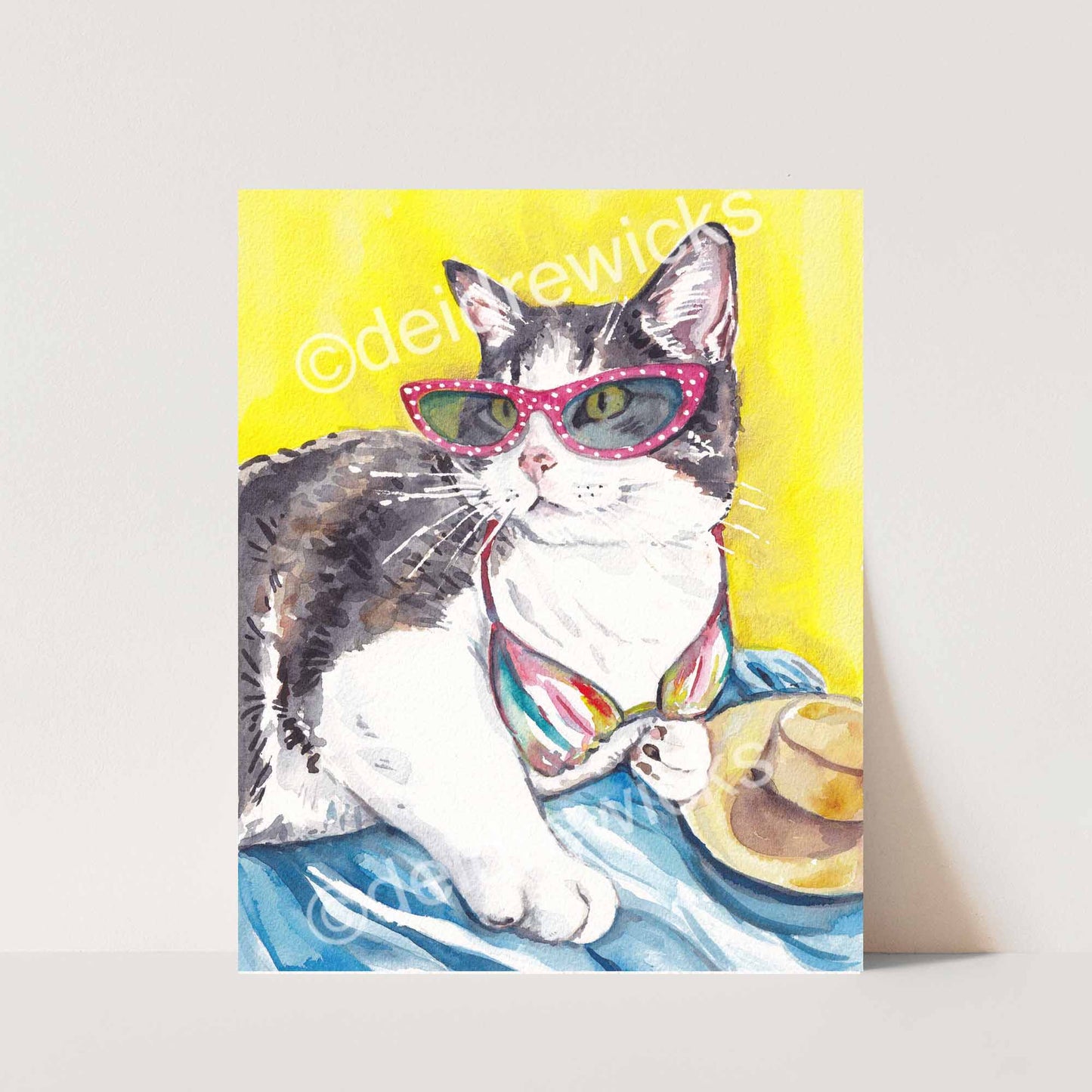 Watercolour painting of a grey tabby cat lying on the beach and wearing vintage cat-eye glasses